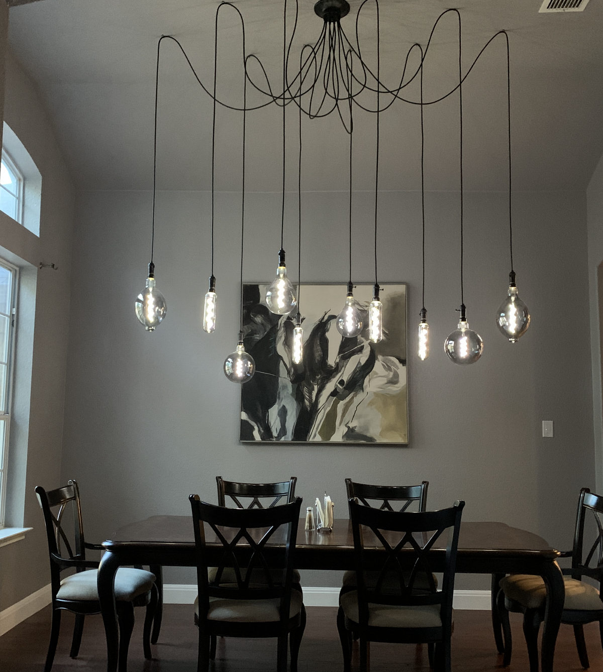 A multi-cord pendant light fixture with large exposed Edison bulbs, hung in a swag pattern from a single ceiling point above a dining table.
